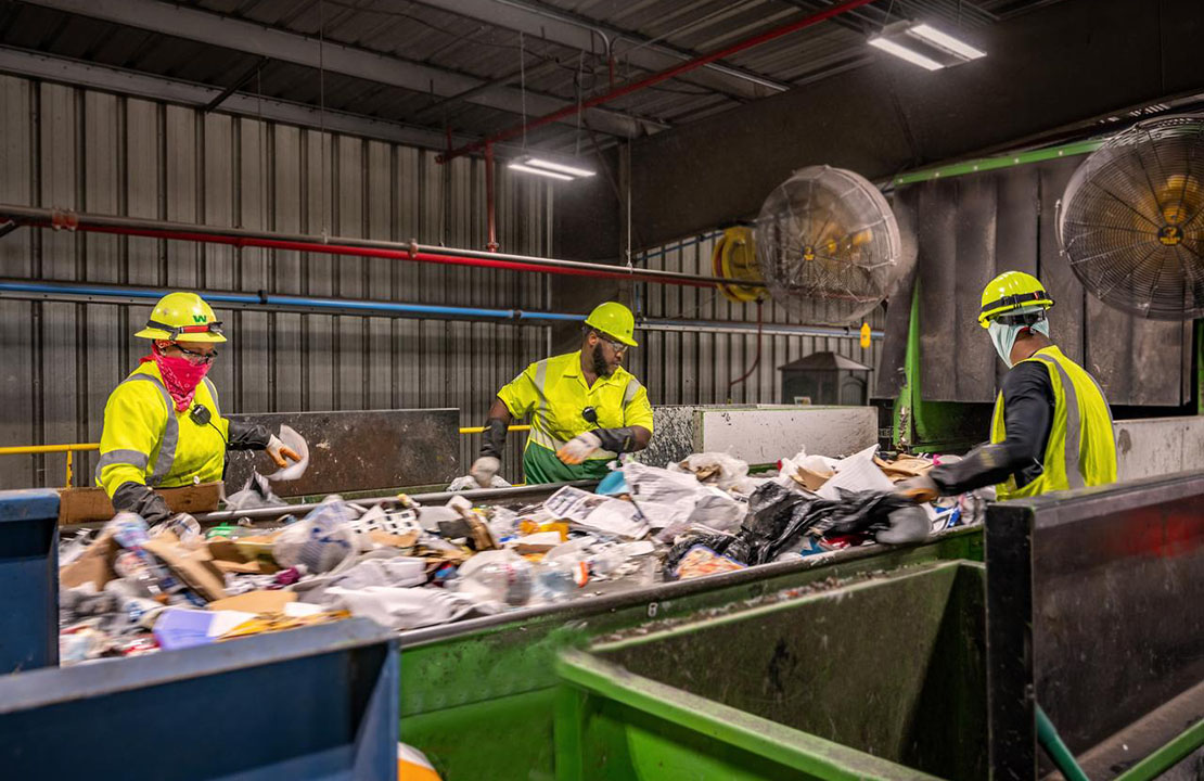 Three WM Recycling Center employees sort recyclables on a conveyor belt