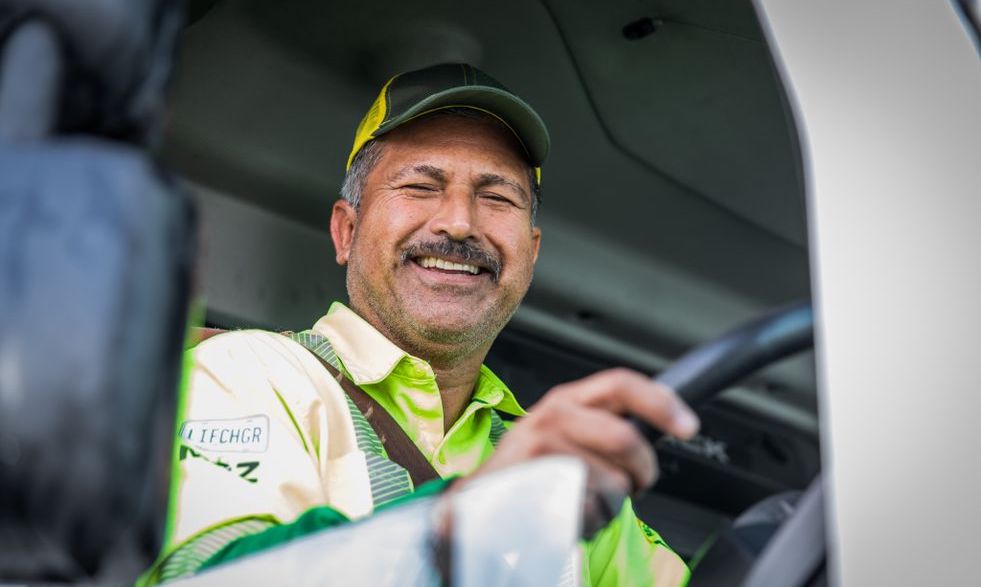 WM driver smiles while operating his trash collection vehicle.